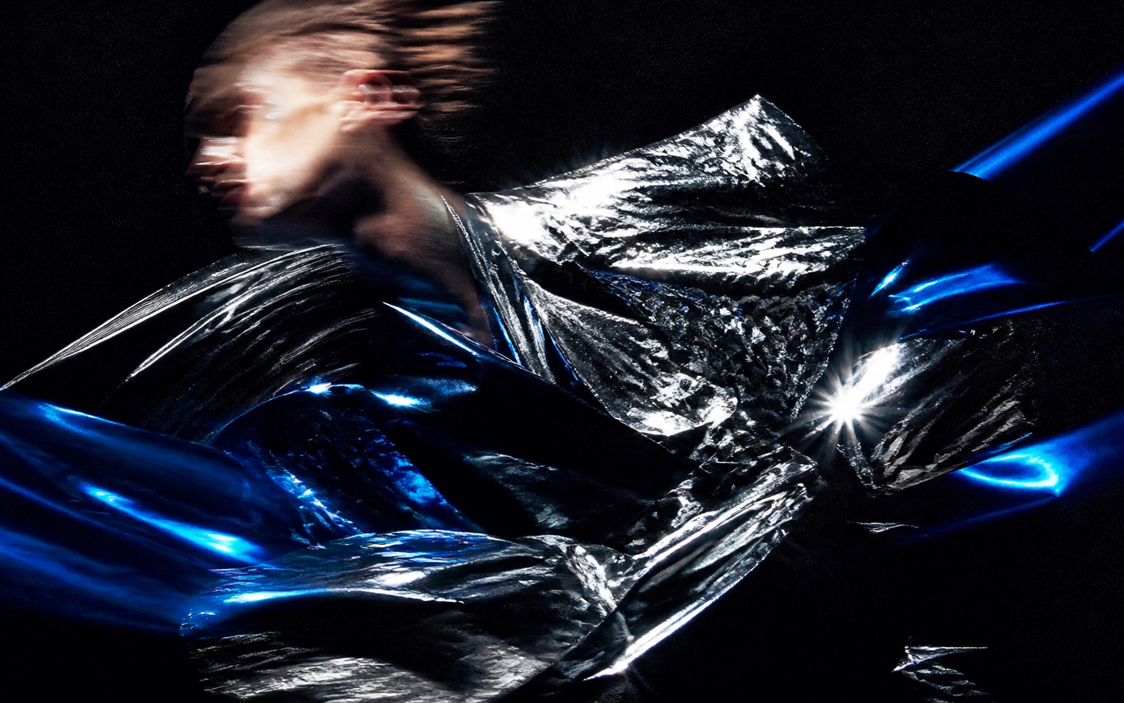A fashion figure moving through chrome fabric and blue light